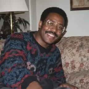 AI-generated portrait of a man in glasses and a patterned knit sweater on a floral sofa in warm lamp light